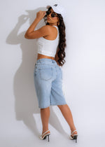  A woman walking down the street wearing Sunset Boulevard Shorts Light Denim, styled with a white tank top and sandals